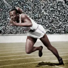 Fotografía en blanco y negro coloreada muestra a Owens con un píe en la pista y otro doblado, inclinado hacia adelante, vestido con camiseta sin mangas y short blancos con rayas delgadas azules y rojas, y zapatillas negras. En el fondo, una multitud en la gradería