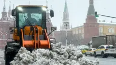 Трактор сгребает кучу снега у стен московского Кремля