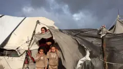 يقف نازحون فلسطينيون أمام خيمتهم بعد تضررها جراء عاصفة في مخيم للنازحين بمدينة غزة، في 13 يناير/كانون الثاني 2026. (تصوير: مجدي فتحي/نورفوتو عبر غيتي إيماجز)