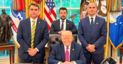 Foto do senador Flávio Bolsonaro, Donald Trump (sentado), Eduardo Bolsonaro (do lado direito) e Paulo Figueiredo sentado atrás de Trump. Todos no salão oval da Casa Branca.