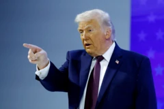 Donald Trump, presidente de Estados Unidos, con un traje azul y una corbata vinotinto se encuentra parado señalando con la mano