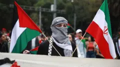 یک تظاهرکننده حامی فلسطین و جمهوری اسلامی که چهره‌اش را پوشانده، دو پرچم جمهوری اسلامی و فلسطین را در دست گرفته است