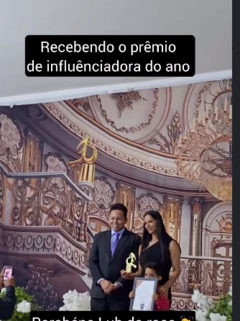 Imagem de duas pessoas em um evento, com um prêmio em forma de diploma