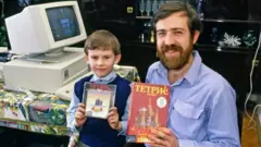 Alexey Pajitnov dan seorang bocah memegang boks tetris.