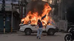 Homem lança objeto em direção a carro que já está em chamas em rua do Nepal