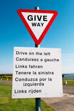 Placa de trânsito orientando as pessoas a trafegar pela mão inglesa, em seis idiomas