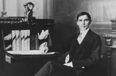 তরুণ মুহাম্মদ আলী জিন্নাহ একটি চেয়ারে হেলান দিয়ে বসে আছেন, একটি হাত পাশের টেবিলে রাখা