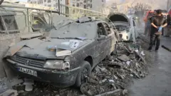 Carros cobertos por escombros nas ruas, com pessoas passando ao lado