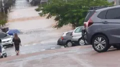Mulher caminhando na rua com guarda-chuva; na frente dela, está grande volume de água