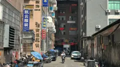 Um homem em uma motocicleta dirige por uma rua com prédios de cada lado
