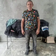 Lázaro Romero León, de pé, olha para a câmera em frente a um pequeno sofá, com jeans escuro e uma camiseta estampada, em um pátio de cimento na cidade de Tapachula, no Estado mexicano de Chiapas
