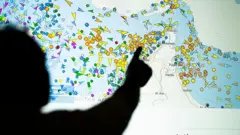 Una persona frente a una gran pantalla que exhibe los movimientos de buques en el estrecho de Ormuz en un sitio web de seguimiento de embarcaciones.