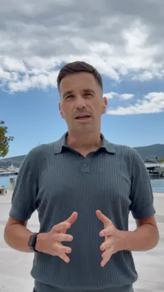 Muškarac gleda u kameru u sivoj majici i gestikulira rukama