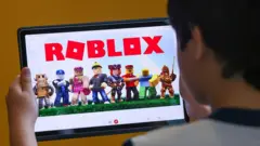 Foto de uma criança de costas segurando um tabelt com o Roblox aberto.