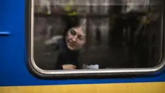 жінка в поїзді виглядає з вікна за склом - поїзд синьо-жовтий