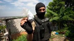 Una agente de policía con pasamontañas y chaleco antibalas exhibe una bolsa de plástico llena de polvo blanco.