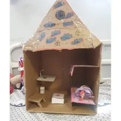 A casa de bonecas feita com papelão e fita adesiva, decorada com cores por Mona, apresenta duas camas de boneca.