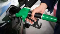 緑色のガスポンプを手に自動車に給油する人