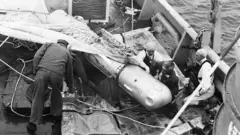 خدمه نیروی دریایی بمب را که تا نیمه در چتر نجات پیچیده شده، یافتند