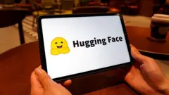 O logotipo do Hugging Face é exibido na tela de um tablet. É um emoji amarelo de um rosto sorridente com as mãos abertas à frente.