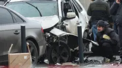 Investigadores trabalham perto de um carro destruído após a explosão de um artefato explosivo.