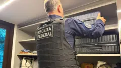 Agente da Receita Federal retira mala de closet em imóvel alvo de mandado de busca e apreensão na Operação Fluxo Oculto