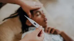 Criança desfocada deitada no sofá; foco está em termômetro