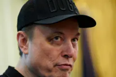 Elon Musk olhando de lado, com boné preto do DOGE