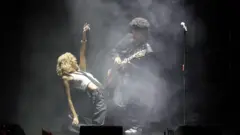Rosé e Bruno Mars cantando e tocando guitarra no palco