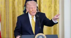 Трамп у синьому костюмі стоїть за трибуною і показує пальцем в сторону 