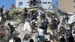 Pesoas buscam sobreviventes entre os escombros de um prédio derrubado pelo terremoto em Cali.