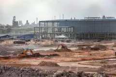 Obra da construção da fábrica da BYD em Camaçari com escavadeiras, pilhas de materiais e estruturas metálicas ao fundo