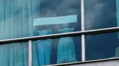 دو دختر پناهجوی افغان پشت پنجره‌ای در یک هتل در پاناماسیتی در حال درخواست کمک 