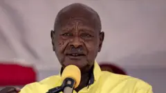Museveni parle dans un micro jaune, vêtu d'une chemise jaune de la même couleur.