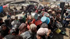 Grupa ljudi sa praznim šerpama čeka da primi humanitarnu pomoć