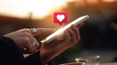 Mão feminina usando celular com ilustração de emoji de coração 
