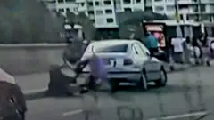 Imagen de un video granulado captado por la cámara de un auto que muestra a dos hombres forcejeando por un arma, uno vestido de negro y el otro de morado.