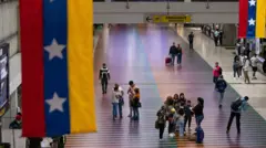 Vista interior del Aeropuerto Internacional de Maiquetía. A los lados hay dos pendones que cuelgan el techo con la bandera de Venezuela y en el centro se ve un pequeño grupo de personas de pie sobre un piso de muchos colores.