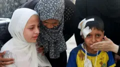 Una madre está junto a sus dos hijos que han resultado heridos en un ataque en Gaza mientras recogían alimentos.