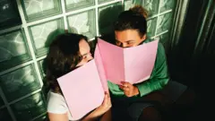 فتاتان تبتسمان خلف دفتريهما