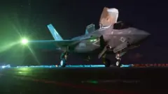 Um caça F-35 americano em um porta-aviões sob um céu noturno