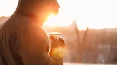 Pessoa tomando uma caneca de café ao ar livre, em dia de sol