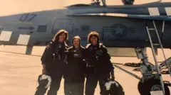 Três mulheres pilotos de caça diante de um avião F/A-18, as três com seus capacetes nas mãos