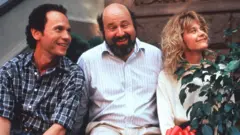 Billy Crystal, Rob Reiner and Meg Ryan sitting together on a step and smiling while filming When Harry Met Sally