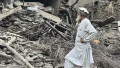 کونړ کې یو سړی له زلزلې وروسته د یوه کور ویجاړیو ته ګوري. 