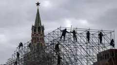 Рабочие монтируют конструкцию сцены на фоне Спасской башни Кремля