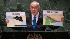Perdana Menteri Israel Benyamin Netanyahu berdiri di podium PBB sambil memegang dua peta di tangannya.