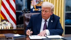 Trump, masasında kararnameleri imzalıyor, arkada Amerikan bayrağı