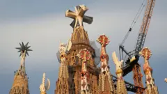 Una foto de las cimas de varias torres ornamentadas, con la más grande en el centro, que tiene una cruz en su parte superior.