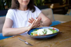 Jovem sentada recusa com as mãos um prato de comida